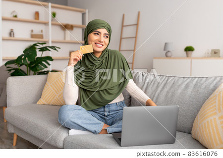 Arab lady in hijab using credit card for remote payment, shopping online via laptop, buying goods in web store at home 83616076