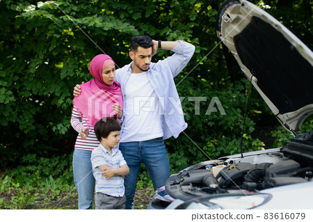 Confused Muslim Family With Little Son Standing Near Broken Car Outdoors 83616079