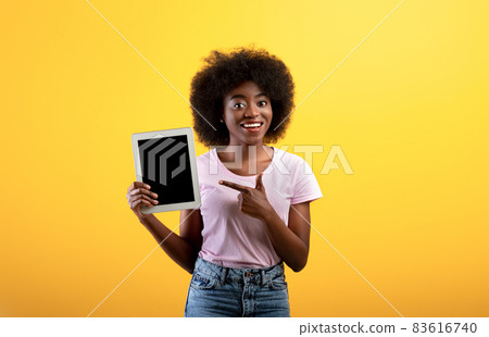 Happy african american lady pointing at digital tablet with blank screen, yellow background, mockup 83616740