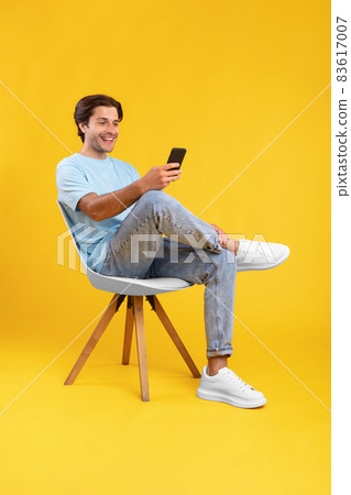 Happy guy using cell phone at studio, sitting on chair Happy guy using cell phone at studio, sitting on chair 83617007