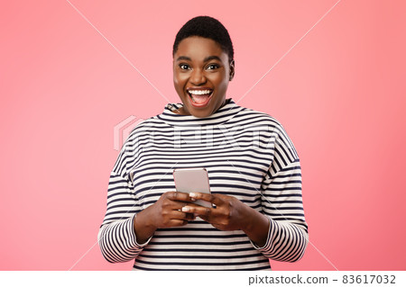Excited Plus Size African Lady Using Mobile Phone Over Pink Background 83617032