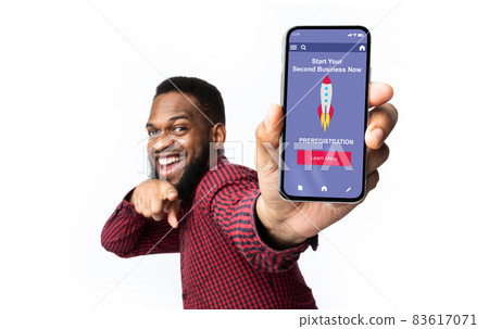 Cheerful young black guy with beard shows finger on phone with website or app about start second business Cheerful young black guy with beard shows finger on phone with website or app about start second business 83617071