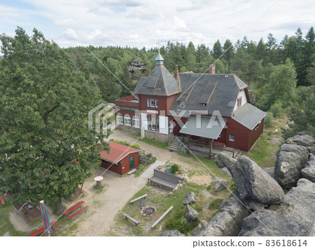 Aerial view of rustic building of Topferbaude restaurant and hut from viewpoint at top of hill Topfer near Oybin at Zittauer Gebirge mountains nature park in Saxony, germany. Summer sunny day Aerial view of rustic building of Topferbaude restaurant and hut from viewpoint at top of hill Topfer near Oybin at Zittauer Gebirge mountains nature park in Saxony, germany. Summer sunny day 83618614