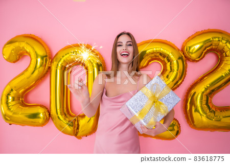 Excited Santa girl raises up sparkle of champagne while holds gift box. 2022 air balloons New Year  83618775