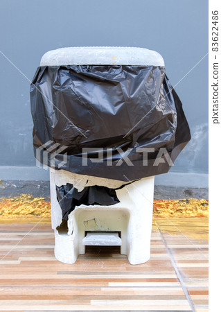 The broken white plastic bin with the black trash bag to use outside the house. The broken white plastic bin with the black trash bag to use outside the house. 83622486