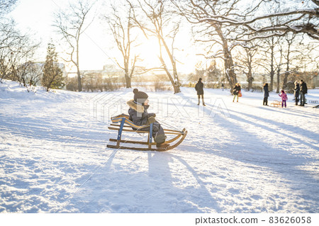Little boy in warm overalls, hat and dumplings riding sled from mountain hill Little boy in warm overalls, hat and dumplings riding sled from mountain hill 83626058