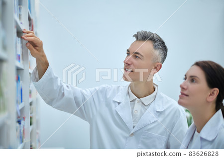 Two pharmacy employees near shelves with medications 83626828