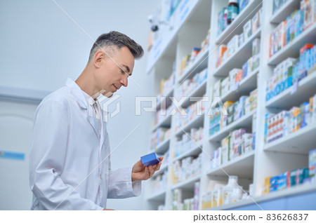 Pleased man in lab coat reviewing medications at pharmacy 83626837
