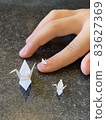 A small white paper crane on the nails of a child's hand and on a table 83627369