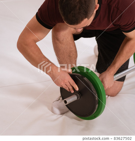 Adding weight to a barbell young man bow on a knee changing black and green plates, equipment for weight training concept. Sports equipment for training. square cropped Adding weight to a barbell young man bow on a knee changing black and green plates, equipment for weight training concept. Sports equipment for training. square cropped 83627502