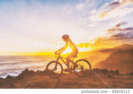 Mountain biking cyclist girl riding MTB bike on coast trail against sunset. Silhouetter of woman doing sports outdoors. Healthy and Active lifestyle. 83628112