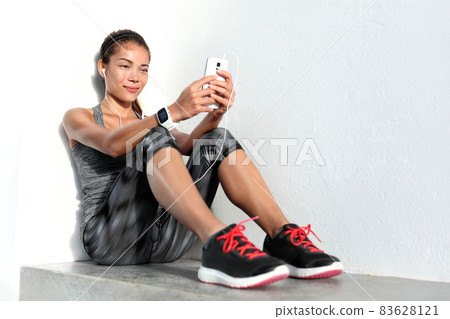 Wearable smart technology devices sport girl lifestyle wearing smartwatch using mobile phone listening to music app with earphones relaxing after fitness workout at gym. Asian woman fit and healthy. Wearable smart technology devices sport girl lifestyle wearing smartwatch using mobile phone listening to music app with earphones relaxing after fitness workout at gym. Asian woman fit and healthy. 83628121