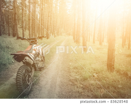 Off-road motorcycle on a forest road. Active rest. Riding a motorcycle in the woods. Solar illumination of the frame. Enduro moto. Selective focus, blur, grain, defocused Off-road motorcycle on a forest road. Active rest. Riding a motorcycle in the woods. Solar illumination of the frame. Enduro moto. Selective focus, blur, grain, defocused 83628548