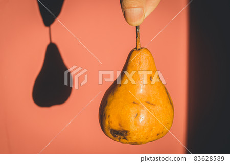 A pear hanging in his hand. Shadow on the wall from a hanging pear. Selective focus, blur, background 83628589