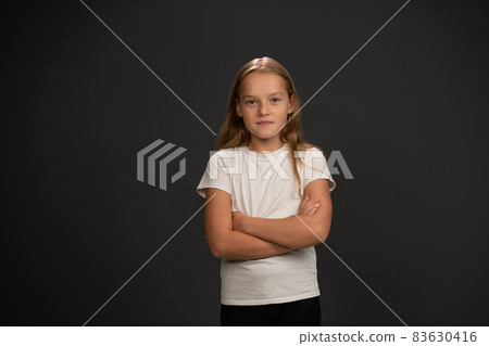 Little girl of 8,10 years with hands folded looks looks questioningly at the camera wearing white t shirt isolated on dark grey or black background Little girl of 8,10 years with hands folded looks looks questioningly at the camera wearing white t shirt isolated on dark grey or black background 83630416