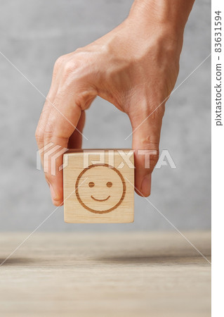 hand holding smile face block. Customer choose Emoticon for user reviews. Service rating, ranking, customer review, satisfaction, mood, mental health and feedback concept 83631594