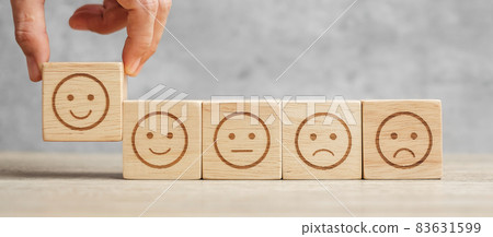 Man hand holding emotion face block. Customer choose Emoticon for user reviews. Service rating, ranking, customer review, satisfaction, mood, evaluation and feedback concept Man hand holding emotion face block. Customer choose Emoticon for user reviews. Service rating, ranking, customer review, satisfaction, mood, evaluation and feedback concept 83631599