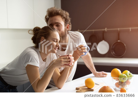 Morning coffee and gentle kissing feeding each other making fun at modern kitchen and smiling while cooking at home. Pretty girl feeds or nursing her boyfriend 83633666