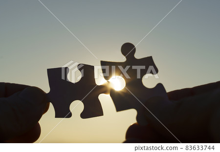 Puzzle pieces are connected. Puzzle pieces in hand on a sunny sky background. Business, partner, solution, alliance, union concept. Puzzle pieces are connected. Puzzle pieces in hand on a sunny sky background. Business, partner, solution, alliance, union concept. 83633744