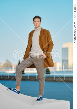 Young man in checkered trousers, sweater and wool coat outdoor 83633892