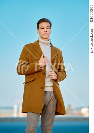 Young man in checkered trousers, sweater wraps wool coat outdoor 83633893