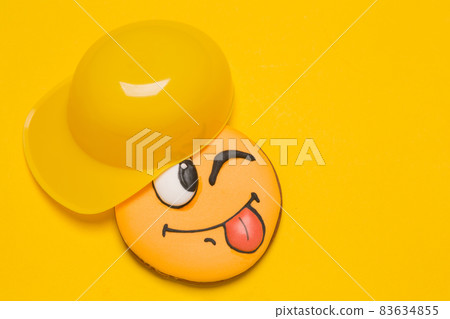 cookie smiley on a yellow background, next to yellow cap baseball cap, baby gingerbread with emotions, concept 83634855