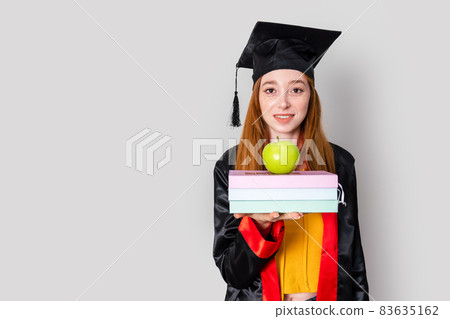 A pretty red haired female student, holding her study books and celebrating her graduation with success. 83635162