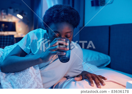 African young woman drinking glass of water before sleeping in the bedroom 83636178