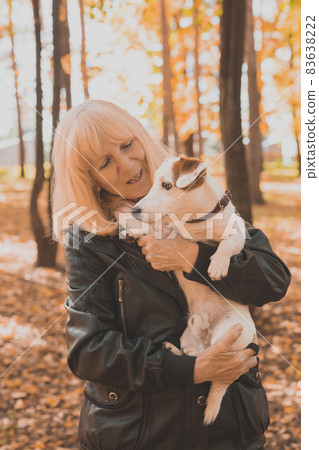 Senior smiling woman hugging her dog in autumn park. Active aging and pet concept. 83638222
