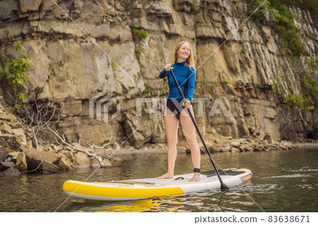 Young women Having Fun Stand Up Paddling in the sea. SUP. Red hair girl Training on Paddle Board near the rocks 83638671