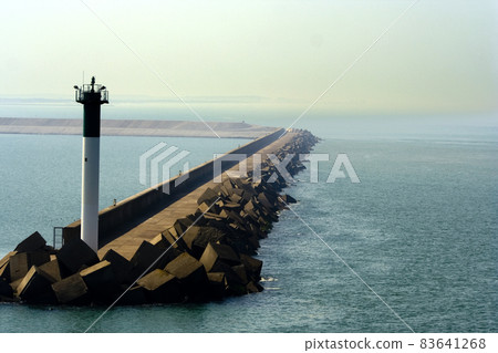 Beacon at the Port of Dunkirk protruding from a pier of cube rocks 83641268