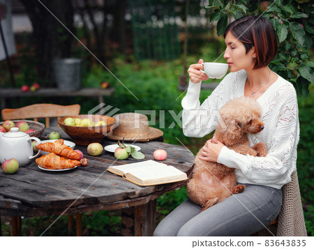 woman having breakfast in garden with her faithful pet poodle. 83643835