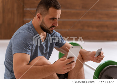 Handsome bearded guy holding debit or credit card in hands using smartphone buying online. Modern digital life. Digital app on smartphone Handsome bearded guy holding debit or credit card in hands using smartphone buying online. Modern digital life. Digital app on smartphone 83644322