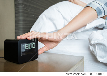 Lazy woman snooze the alarm clock. 83644803