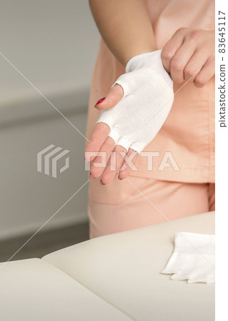 Cosmetologist in workwear wearing white bamboo fingerless gloves on her hands. Cosmetologist in workwear wearing white bamboo fingerless gloves on her hands. 83645117