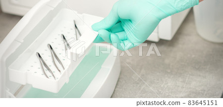 The beautician holds a tray of tweezers preparing them for disinfection with a special liquid and machine. The beautician holds a tray of tweezers preparing them for disinfection with a special liquid and machine. 83645151