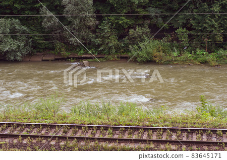 Railroad among mountains covered with dense forest, flowing mountain river. Railroad among mountains covered with dense forest, flowing mountain river. 83645171