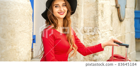 Beautiful young caucasian woman in black hat smiling and sitting on stairs at the door outdoors. 83645184