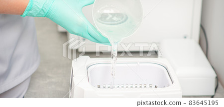The beautician adds liquid for disinfection of instruments to the machine for sterilization of tools. The beautician adds liquid for disinfection of instruments to the machine for sterilization of tools. 83645195