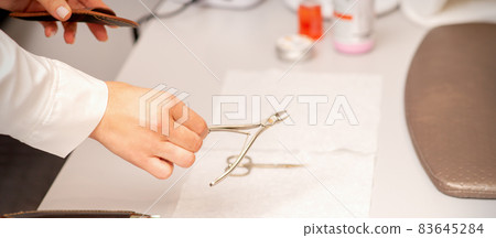 Nail nippers in the hand of female manicure master putting to the towel before nail care in manicure salon. 83645284