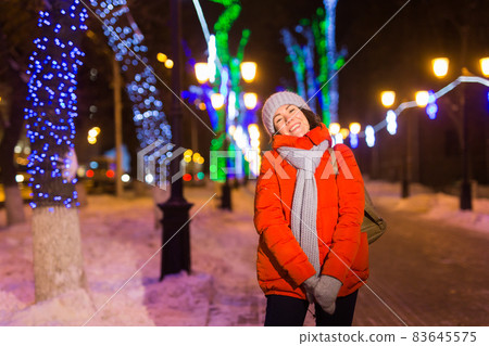 Happy funny young woman with winter clothes background evening city lights illumination. Christmas and winter holidays concept. Happy funny young woman with winter clothes background evening city lights illumination. Christmas and winter holidays concept. 83645575