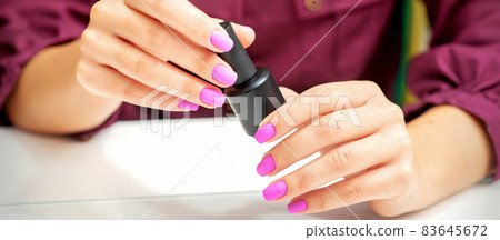 White woman holding nail polish black bottle with painted pink nails close up. White woman holding nail polish black bottle with painted pink nails close up. 83645672