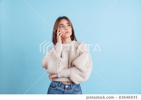 Portrait of young beuatiful girl, student in casual clothes looking up isolated on light blue studio backgroud Portrait of young beuatiful girl, student in casual clothes looking up isolated on light blue studio backgroud 83646935