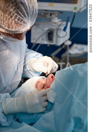 Close up of the face of a patient who is undergoing blepharoplasty. The surgeon cuts the eyelid and performs manipulations using medical instruments 83647820
