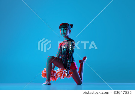 Full-length portrait of beautiful girl, cheerleader training, performing in bright bodysuit with pom-pons isolated over blue background in neon lights Full-length portrait of beautiful girl, cheerleader training, performing in bright bodysuit with pom-pons isolated over blue background in neon lights 83647825