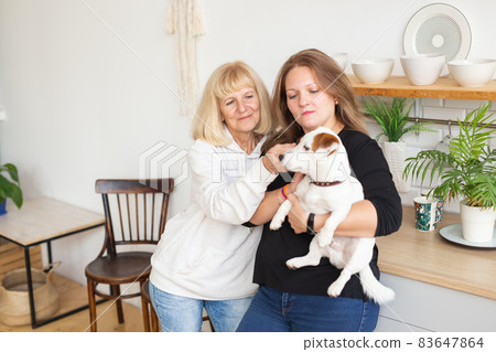 Senior woman with adult daughter relaxing at home. Woman holds her jack russell terrier dog. Family concept 83647864