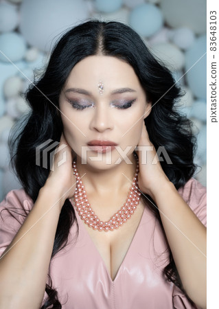 Caucasian Pretty Woman With Closed Eyes Put Her Hands Behind Her Head. Portrait of a Sexy Brunette Lady with Beauty Face. Close-up. Pastel Balls Background 83648103