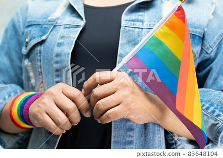 Asian lady wearing blue jean jacket or denim shirt and holding rainbow color flag, symbol of LGBT pride month celebrate annual in June social of gay, lesbian, bisexual, transgender, human rights. Asian lady wearing blue jean jacket or denim shirt and holding rainbow color flag, symbol of LGBT pride month celebrate annual in June social of gay, lesbian, bisexual, transgender, human rights. 83648104