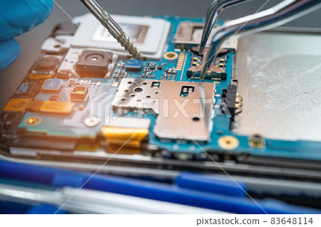 Technician repairing inside of mobile phone by soldering iron. Integrated Circuit. the concept of data, hardware, technology. Technician repairing inside of mobile phone by soldering iron. Integrated Circuit. the concept of data, hardware, technology. 83648114