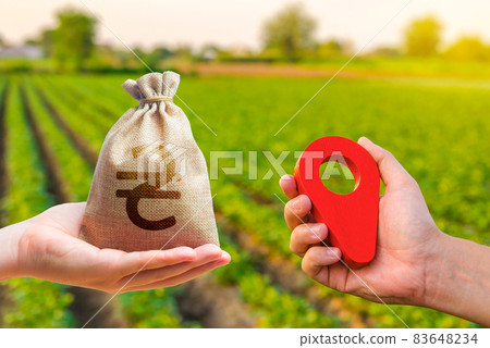 Hands with location pin and ukrainian hryvnia money bag. Land market. Estimation cost of plots. Agriculture agribusiness. Transport and construction industry. Buying and selling land. 83648234
